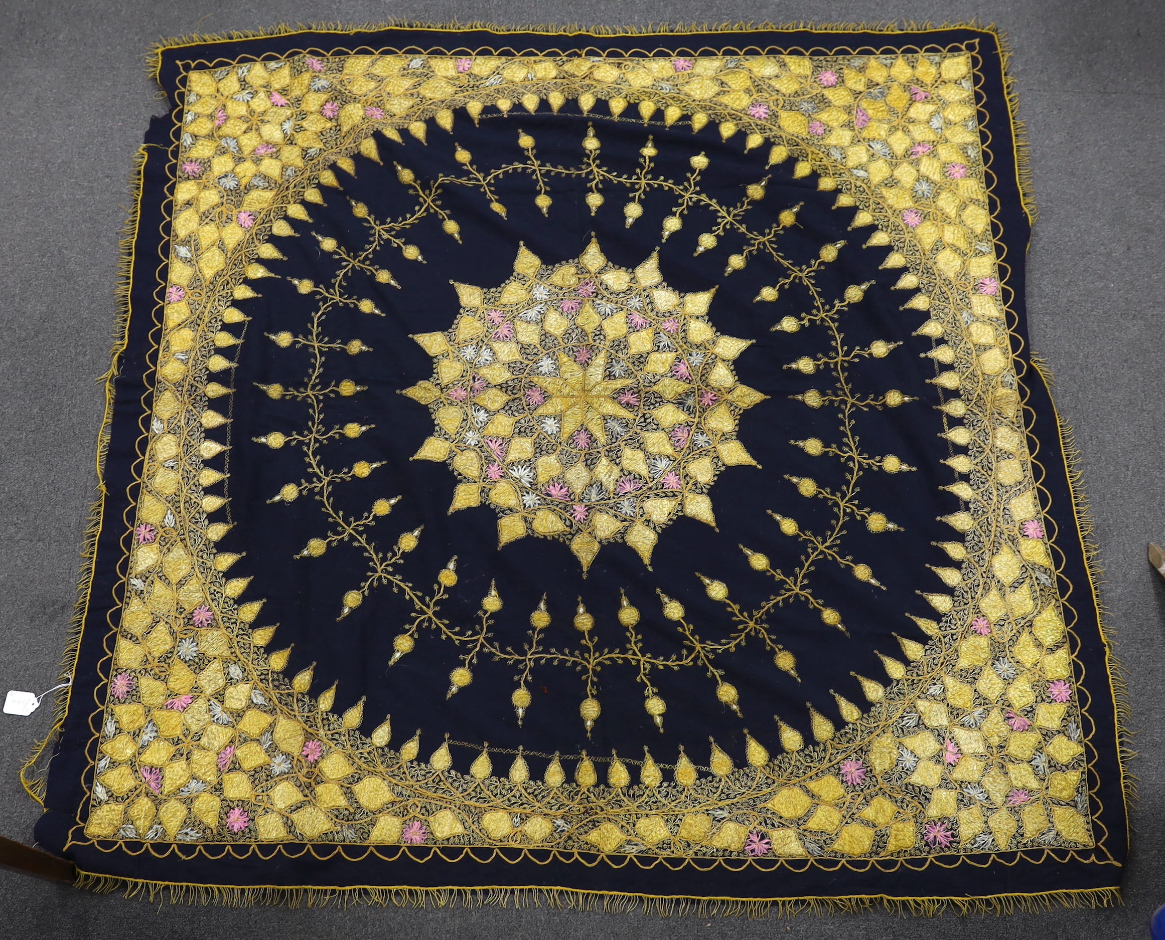 An Indian gold thread and coloured silk floss embroidered black wool cover with gold thread fringing and a later woven cover with bobble edging, black and gold cover 172cm x 169cm